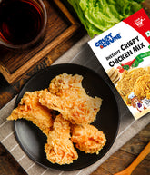 Crispy chicken pieces on a plate with a box of Crust & Crumb instant crispy chicken mix-hot & spicy and a glass of red wine.
